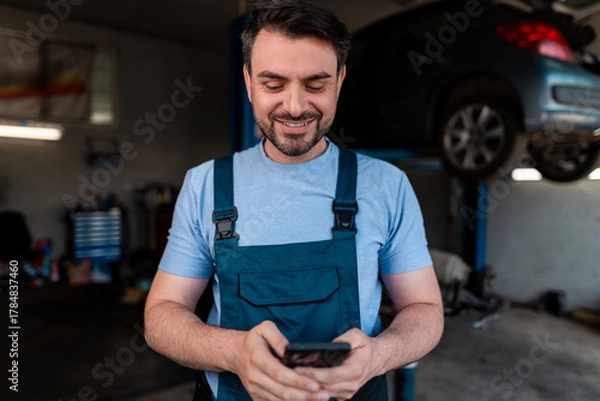 Fototapeta Mechanic checks phone while working in an auto repair shop during the day