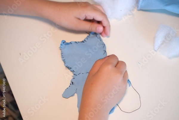Fototapeta Top view. Children's hands hold a needle and thread and learn to sew.