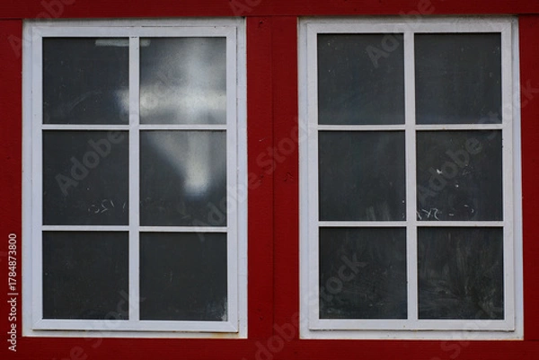 Fototapeta Two white lattice windows with dark red frames set in a red brick wall, highlighting a classic architectural feel.