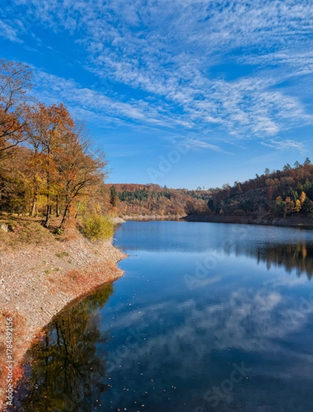 Obraz the Sengbach dam with reflections of the blue sky in the sunshine and the colorful autumn forest