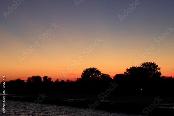 Fototapeta Twilight view of a calm shoreline with silhouetted trees