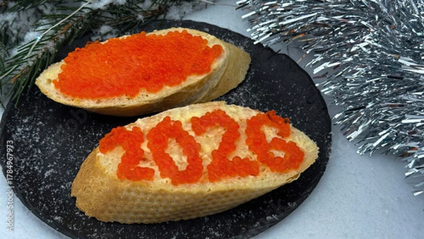 Fototapeta A sandwich 2026 with red caviar and a glass of champagne against the backdrop of a snowy Christmas tree.