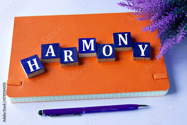 Fototapeta HARMONY - a word written on wooden cubes on an orange notepad with a pen lying nearby
