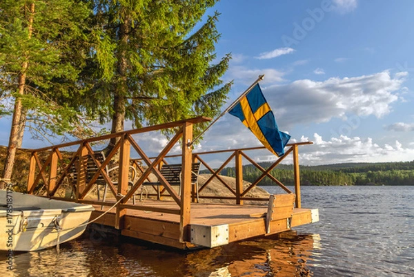 Fototapeta Swedish flag flying over wooden dock on serene lake