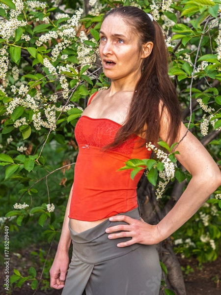 Obraz Young woman sneezes in the park against the background of a flowering tree. Allergy to pollen concept.