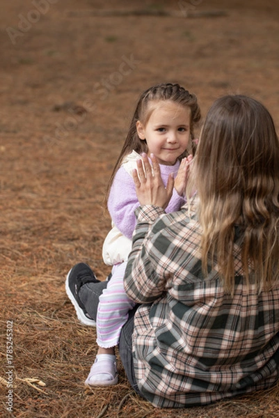 Fototapeta Mother and daughter playing patty-cake together while sitting in a pine forest.