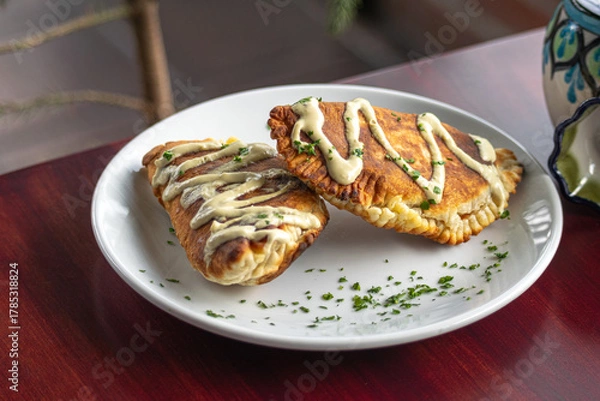 Fototapeta Close-up photograph from above of fried empanadas with sauce on a white spiced plate on a Corinthian table