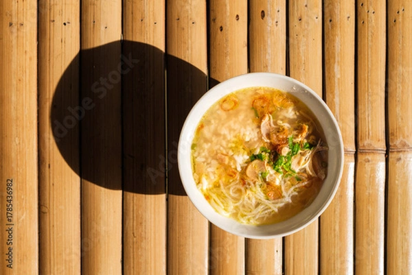 Obraz Overhead shot of nusantara indonesian food calles soto filled with chicken noodle soup in a white bowl, placed on a bamboo mat with a shadow.