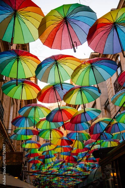 Fototapeta Colorful umbrellas create a vibrant atmosphere in a narrow street in an urban area during dusk