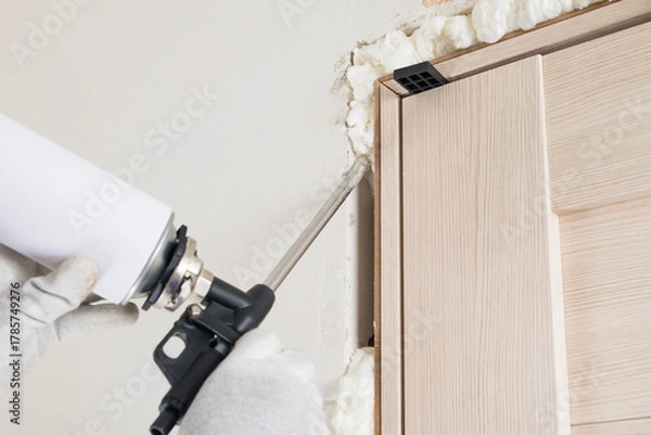 Obraz The use of mounting foam by a worker to seal cracks and mounting wedges for mounting, close-up