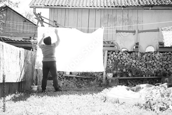 Fototapeta Monochrome shot captures a person hanging laundry in a backyard, showcasing domestic tasks and simple rural living in black and white.