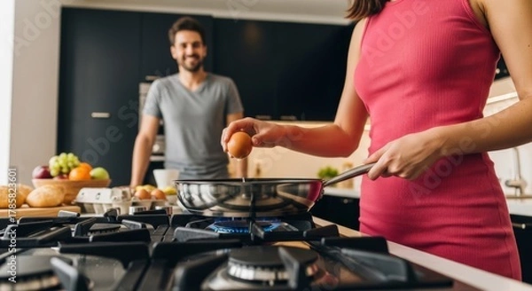 Fototapeta Culinary Creation: A woman expertly cracks an egg into a sizzling pan, while a man smiles in anticipation, the essence of home-cooked meal is a focus of togetherness and simplicity.
