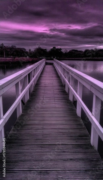Fototapeta A serene view of a wooden bridge stretching across calm water under a dramatic sky, creating a pathway to tranquility and reflection.