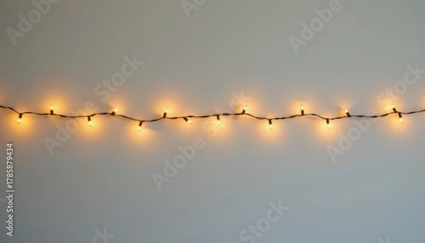 Obraz Warm white string lights illuminate a plain light gray wall with empty space above