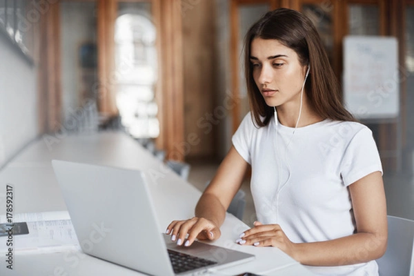 Fototapeta Young woman using a notebook computer watching streaming movies or listening to online music in university campus.