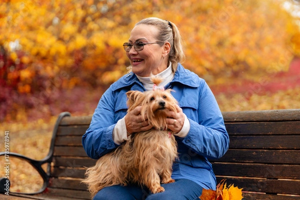 Fototapeta Smiling woman enjoys time with small dog in colorful autumn park