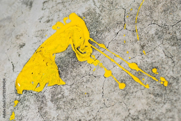 Fototapeta A dynamic splatter of bright yellow paint contrasts sharply against a cracked and textured grey concrete surface