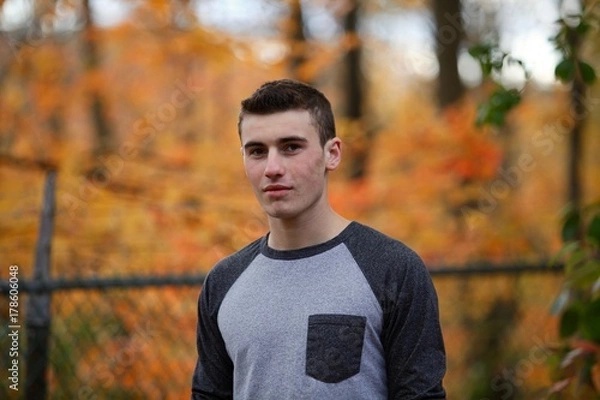 Fototapeta Portrait head shot of a teenage boy outside in front of an orange tree in autumn