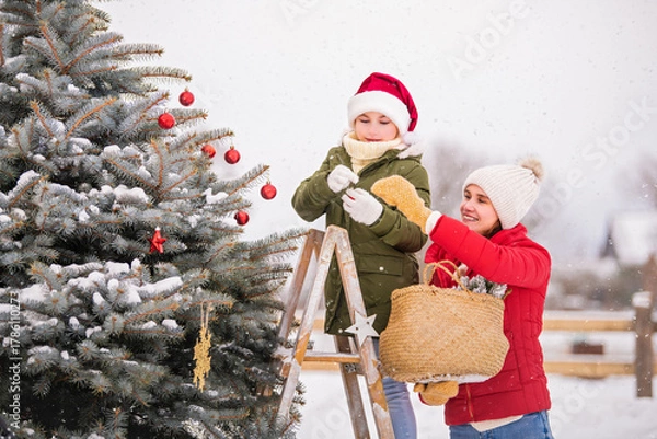 Obraz mother and the daughter decorate a Christmas tree snowy winter outside