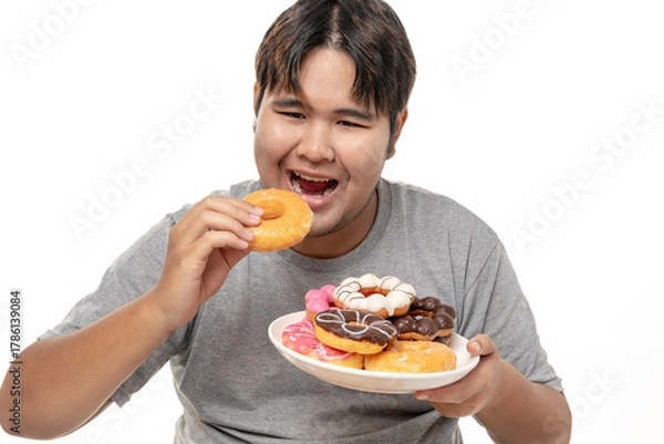 Fototapeta Young Asian fat man is enjoying eating delicious donuts on white background, tudio shot.