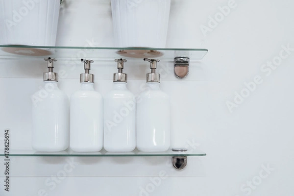 Fototapeta Bathroom soap dispenser and pot on shelf with white background of negative space horizontal..White ceramic bottles with liquid soap or shower gel at hotel.