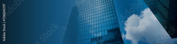 Fototapeta Modern glass skyscraper reflecting bright blue sky and clouds, creating a professional corporate business background ideal for finance, real estate, and commercial branding.