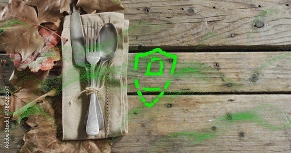 Fototapeta Placing beige napkin with three utensils and twine on wooden tabletop, green shield, copy space