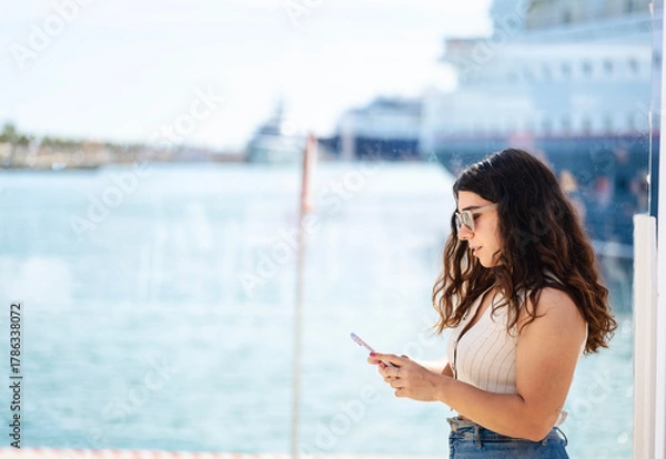 Obraz Smiling woman looking at her cell phone in the harbor
