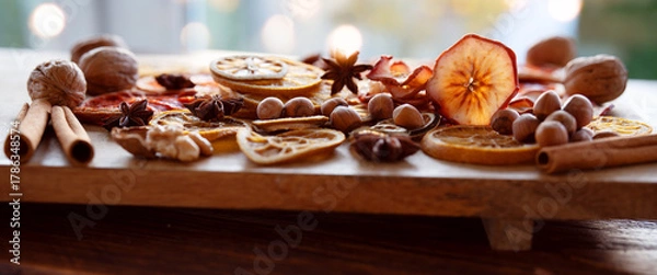 Fototapeta Dried citrus fruits and apple rings with nuts on rustic wood for the christmas. Preparations for christmas hot drinks.