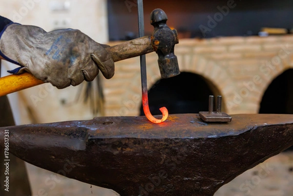 Obraz Blacksmith hammering glowing metal while forging hook