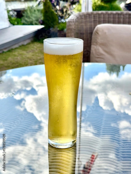 Obraz Pint glass of cold golden lager beer on a table in the garden of a luxury hotel. No people.