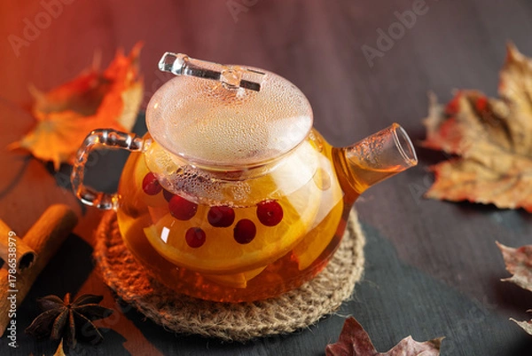 Fototapeta Tea with red berries, orange and spices in a teapot on a wooden table with autumn dry leaves