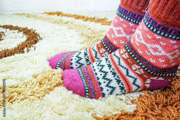 Fototapeta Female feet in warm socks with Nordic ornament resting on soft carpet surface. Reflects sustainable fashion, slow craft movement, natural materials, winter hygge mood, and calm domestic atmosphere.