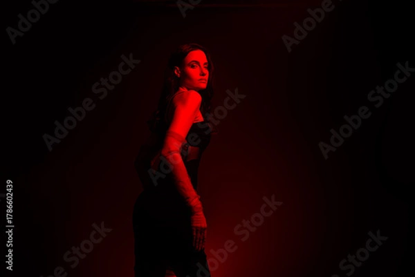 Fototapeta Young elegant woman in red lighting setting posing for stylish photoshoot with an aura of sensuality and glamour