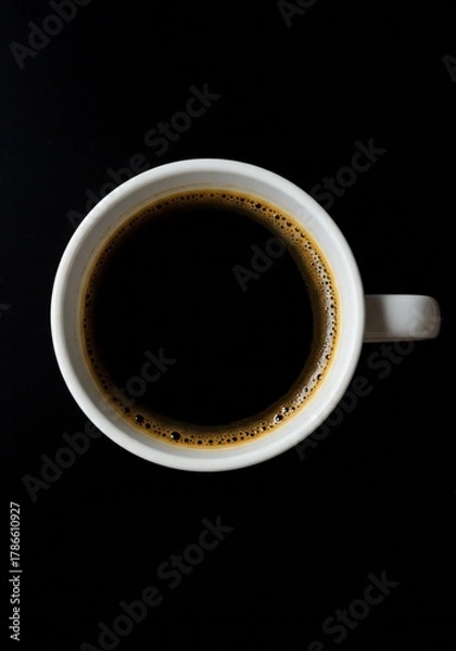 Fototapeta A top-down view of a white coffee cup filled with dark coffee, set against a black background.