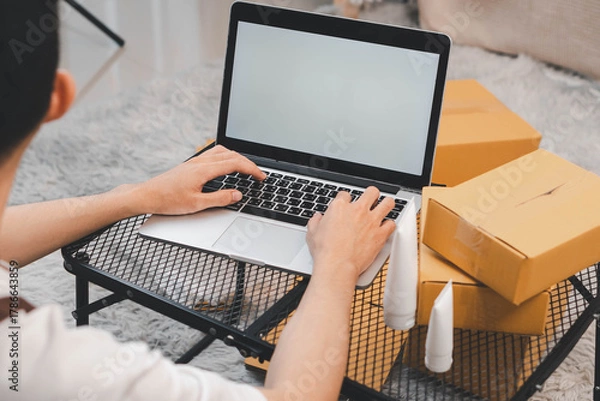 Fototapeta Startup small business owner packing boxes for online customer delivery. Entrepreneur managing e-commerce orders, shipping parcels, and running home-based business operations from home office.