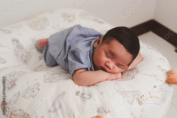 Fototapeta Cute newborn baby boy sleeping peacefully in white crib and soft nest. Close-up of infant resting on bed, symbolizing childhood innocence, comfort, and family love. Perfect for baby care themes.
