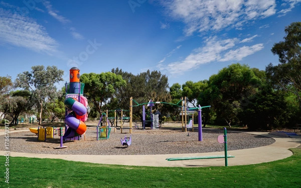 Fototapeta Colorful playground equipment in a sunny park with spiral slide and climbing structure