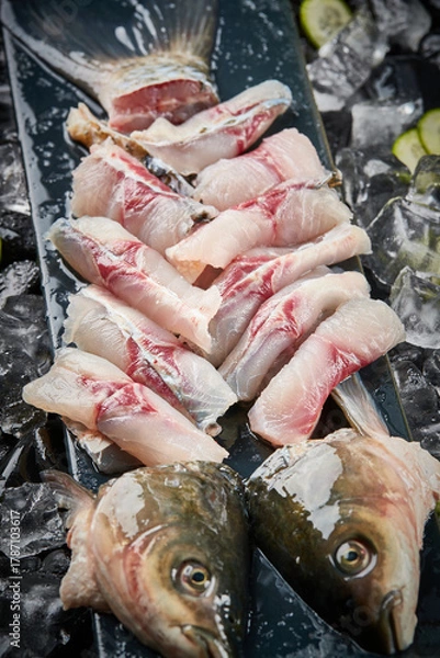 Fototapeta Arrange the glistening, white slices of fresh fish on a black round porcelain plate.