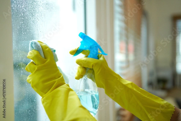 Fototapeta Person wearing yellow gloves cleaning a window with a spray bottle and cloth