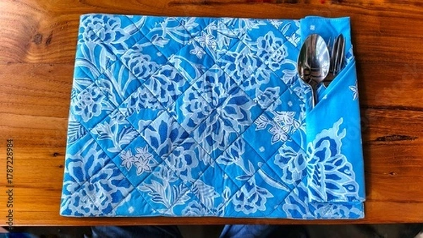 Obraz A blue and white patterned placemat with silverware on a wooden table.