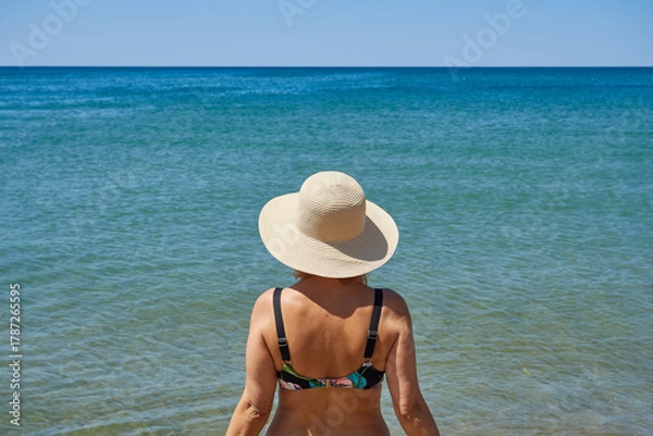 Fototapeta Close-up rear view of a mature woman standing by the sea. Concept of relaxation, travel.