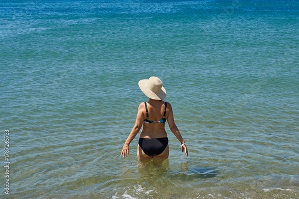 Fototapeta Rear view of a retired woman in a swimsuit getting ready to swim in the sea