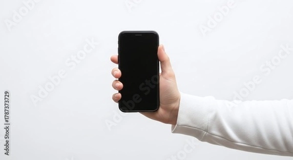 Fototapeta A hand holding a black smartphone with a blank screen against a plain white background in a studio shot