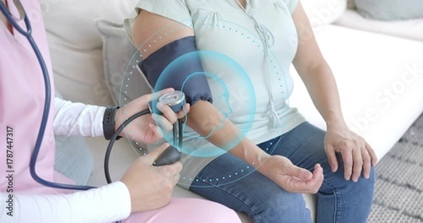 Obraz Measuring pink-scrub nurse applying BP cuff to patient in mint blouse at home, with overlay