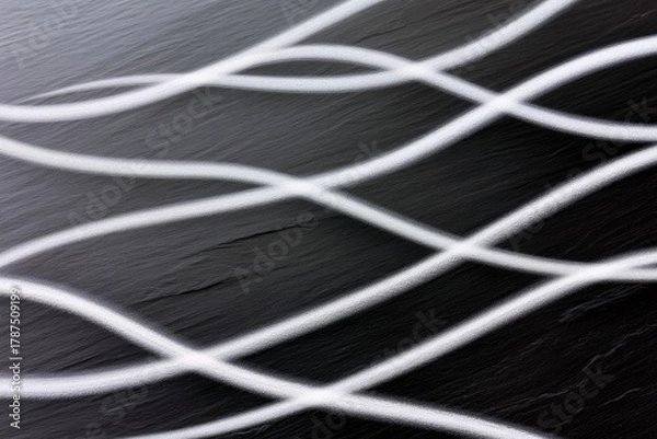 Fototapeta A dark, textured surface is overlaid with flowing, white, wavy lines that intersect and create a dynamic, abstract pattern.