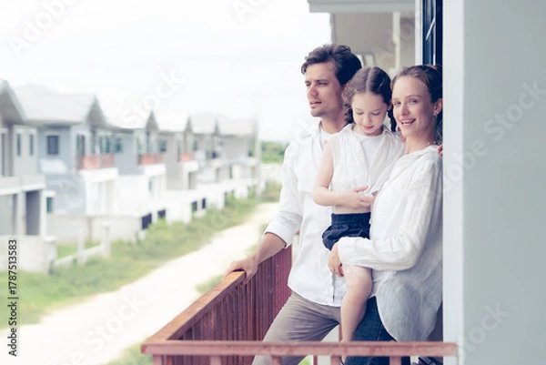 Fototapeta A loving couple and their child stand together on a balcony, gazing at a developing residential area. This picture evokes feelings of aspiration, family values, and planning for the future.