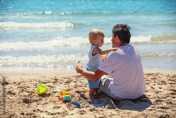 Fototapeta A happy grandfather and his little grandson are playing on the beach. Grandfather is holding the child in his arms