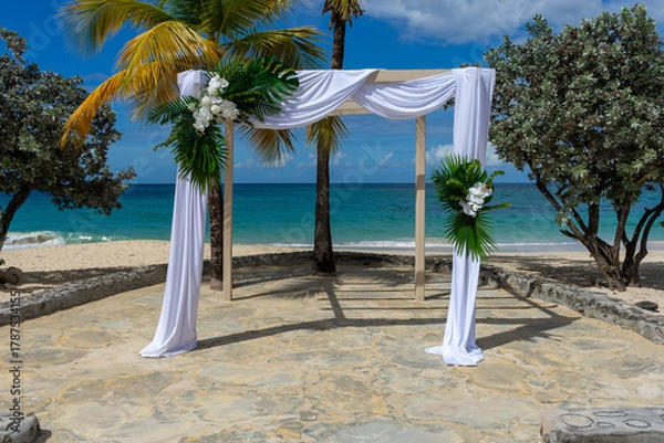 Obraz A silk-draped wedding pagoda adorned with white Phalaenopsis aphrodite orchids and lush tropical foliage stands on a Caribbean beach against the turquoise sea