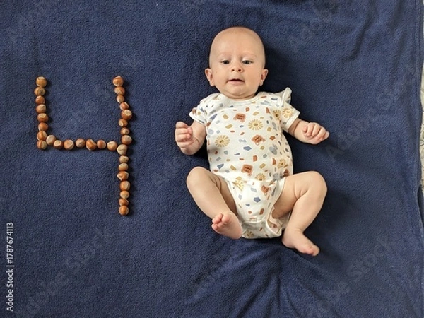 Fototapeta Adorable four-month-old baby celebrating a milestone, lying next to the number four made of walnuts.

